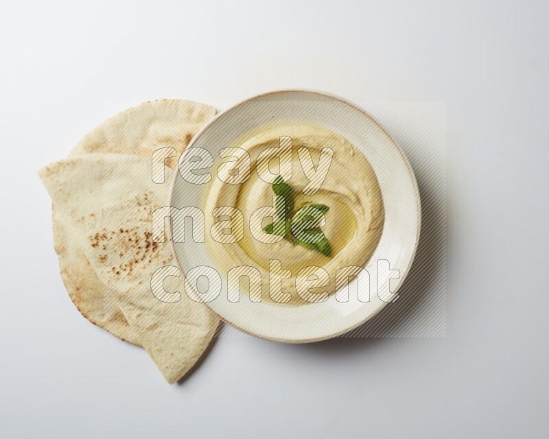 Hummus in a pottry plate garnished with mint  on a white background