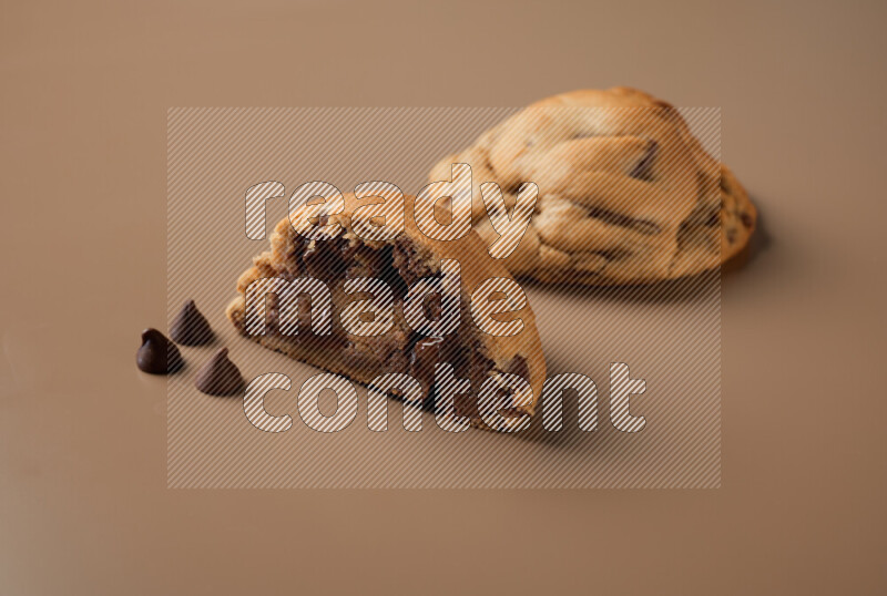 a chocolate chip cookie with another one cut in half on a brown background