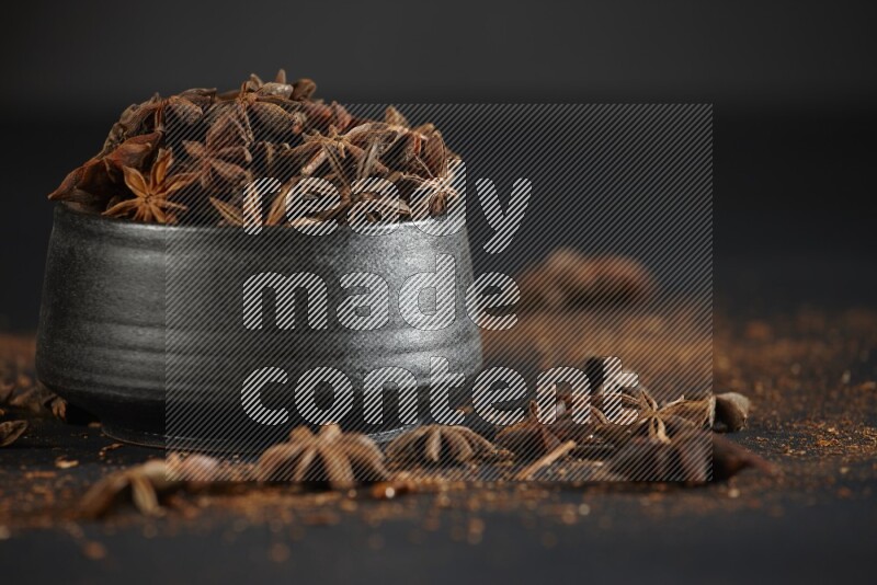 Star Anise in a black bowl with sprinkled anise on black flooring
