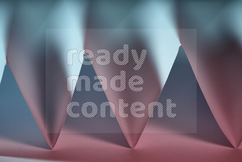 A close-up abstract image showing sharp geometric paper folds in blue and pink gradients