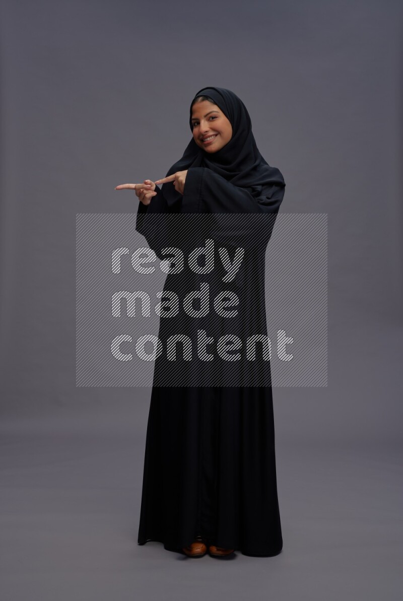Saudi woman wearing Abaya standing interacting with the camera on gray background