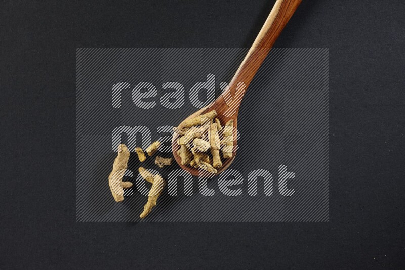 A wooden ladle full of dried turmeric fingers on black flooring