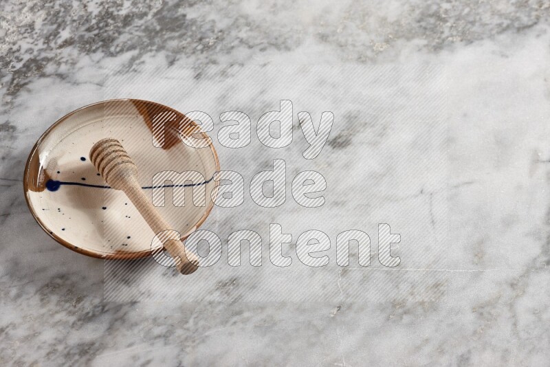 Multicolored pottery plate with wooden honey dipper in it on grey marble background