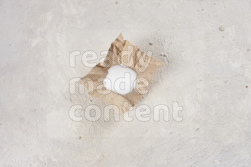 A crumpled piece of paper full of white salt on white background