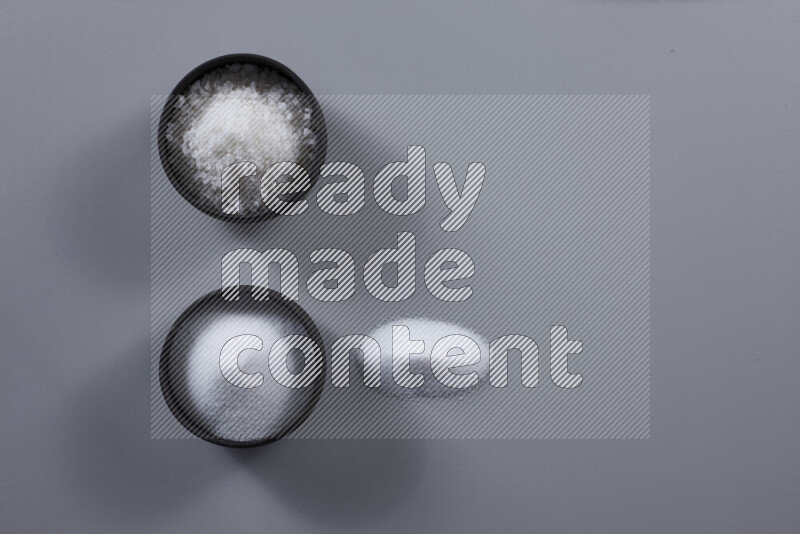 2 وعاء فخاري احدهمها ممتلئ بملح الطعام الأبيض والأخر بملح البحر الخشن على خلفية رمادية