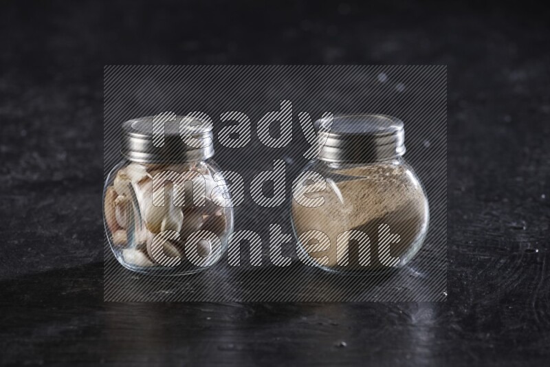 2 glass spice jars full of garlic powder and cloves on a textured black flooring