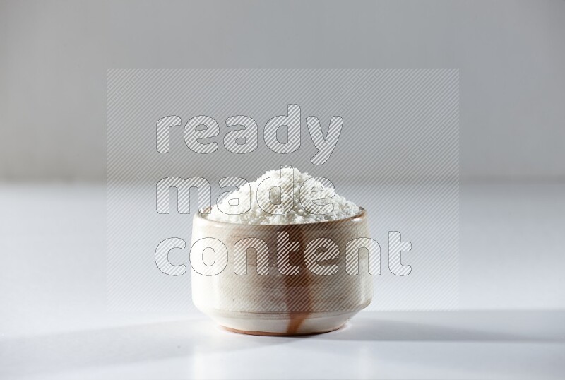 A beige ceramic bowl full of desiccated coconut on a white background in different angles
