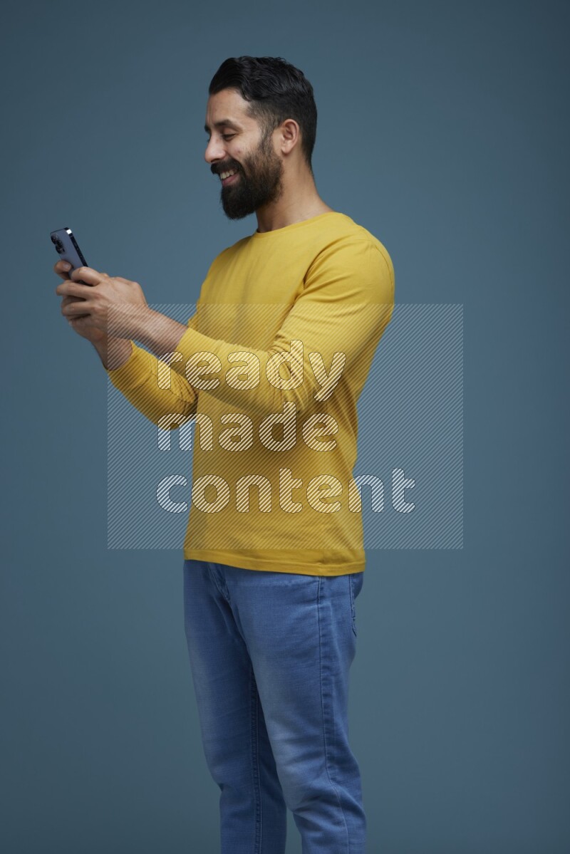 Man typing on his phone in a blue background wearing a yellow shirt