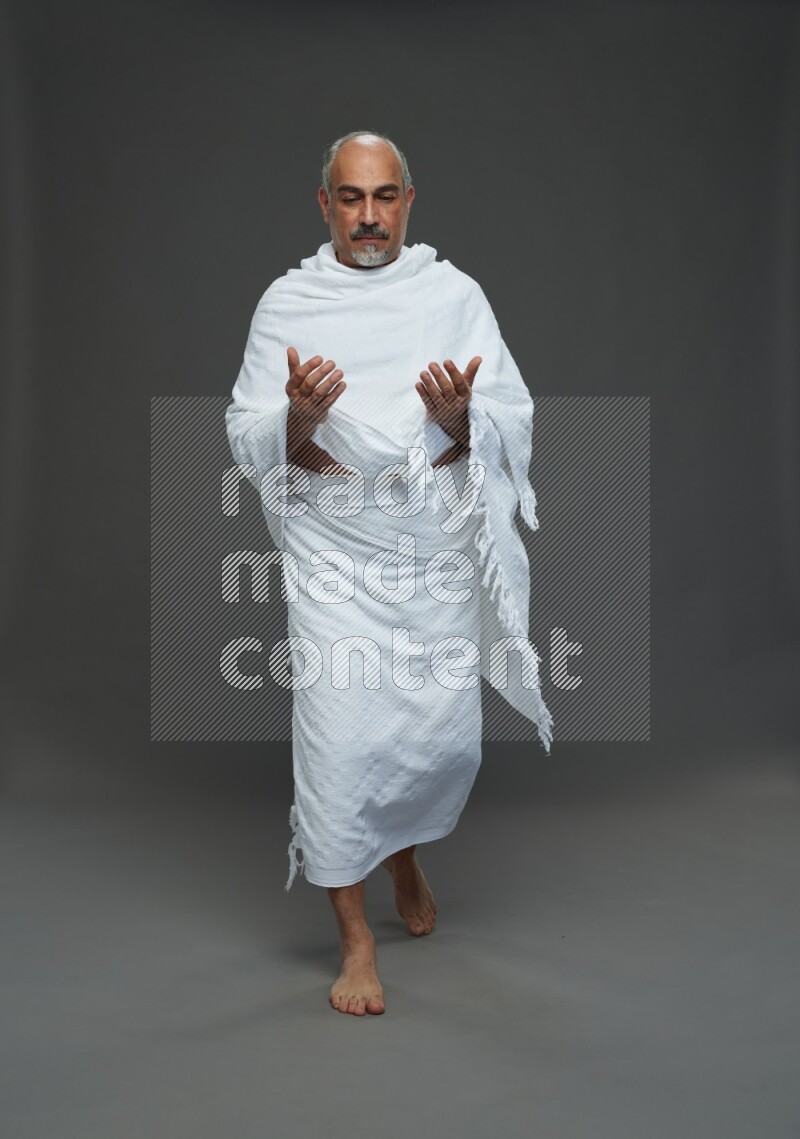 A man wearing Ehram Standing dua'a on gray background