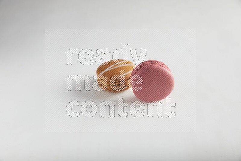 45º Shot of of two assorted Brown Irish Cream, and Pink Raspberry macarons on white background