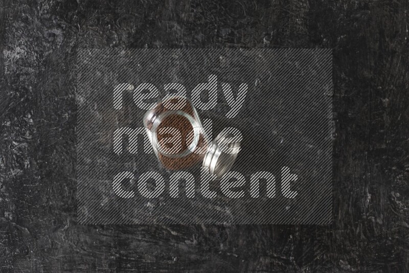 وعاء بهارات زجاجي ممتلئ ببودرة القرنفل على أرضية سوداء