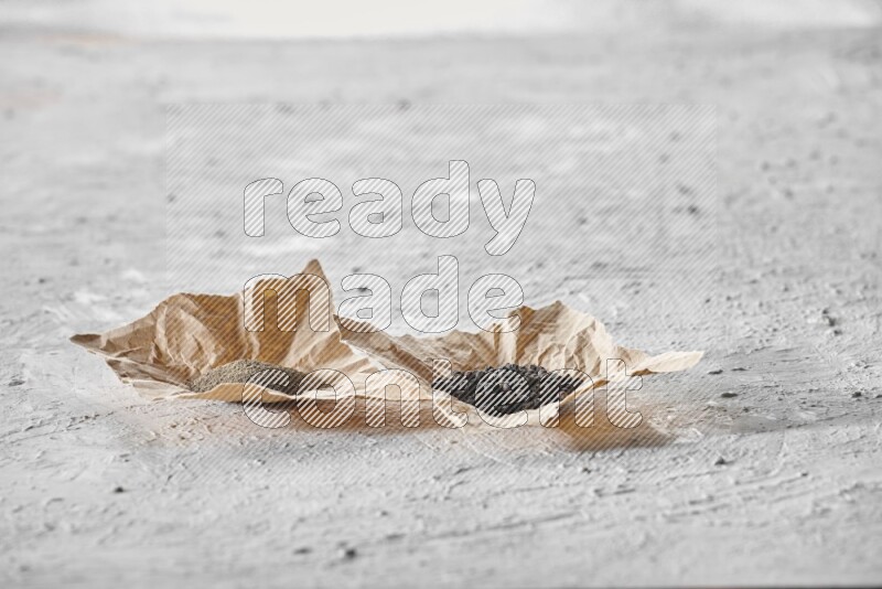 Black pepper and black pepper powder on 2 crumpled pieces of craft paper on a textured white flooring