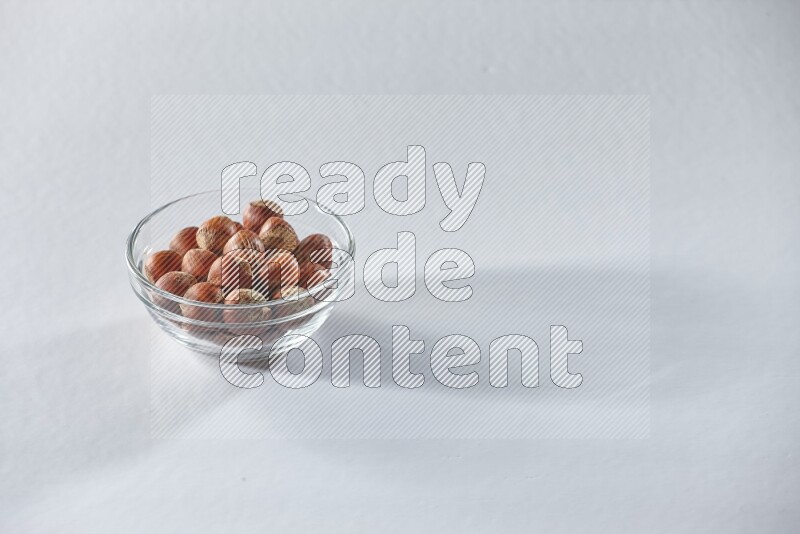 A glass bowl full of hazelnuts on a white background in different angles