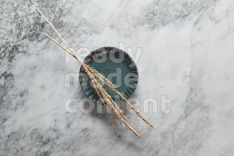 Wheat stalks on multicolored pottery plate on grey marble background
