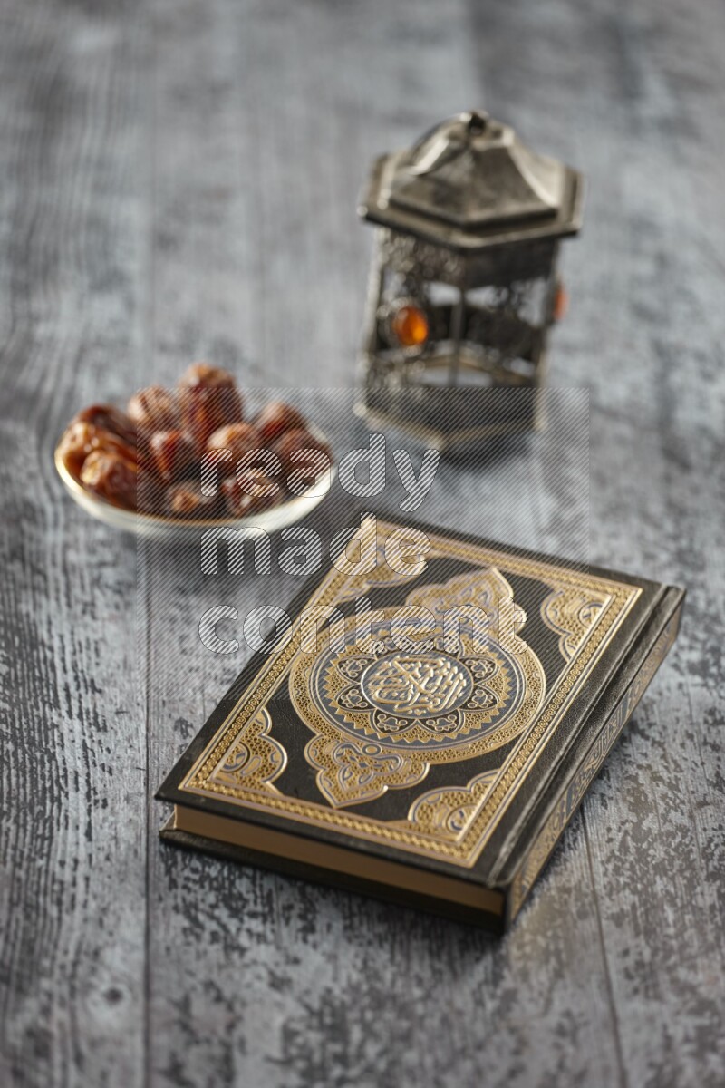 A silver lantern with different drinks, dates, nuts, prayer beads and quran on grey wooden background