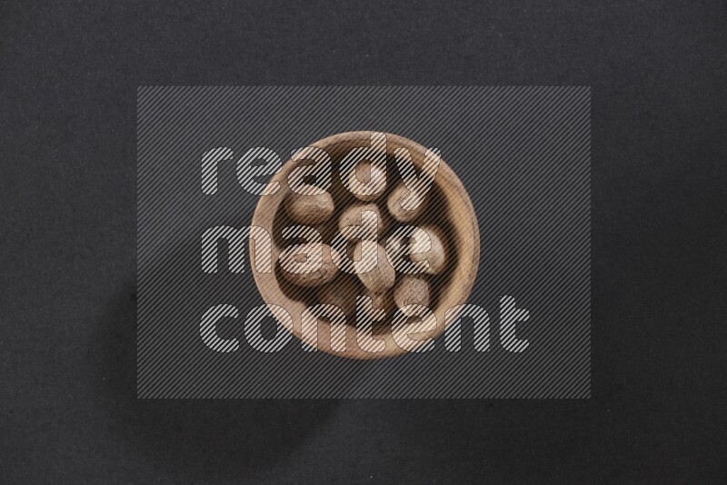 A wooden bowl full of whole nutmeg seeds on a black flooring