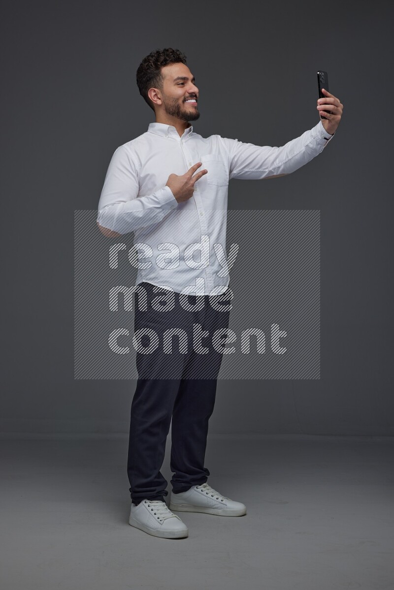 A man wearing smart casual and taking selfie with his phone eye level on a gray background