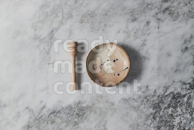 Multicolored pottery bowl with wooden honey dipper on the side on grey marble background