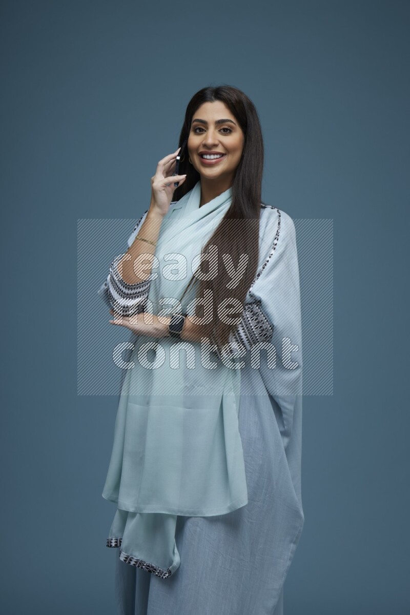 A Saudi woman having a Call in a blue background wearing a blue Abaya with no hijab