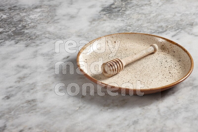 Beige pottery plate with wooden honey dipper in it on grey marble background