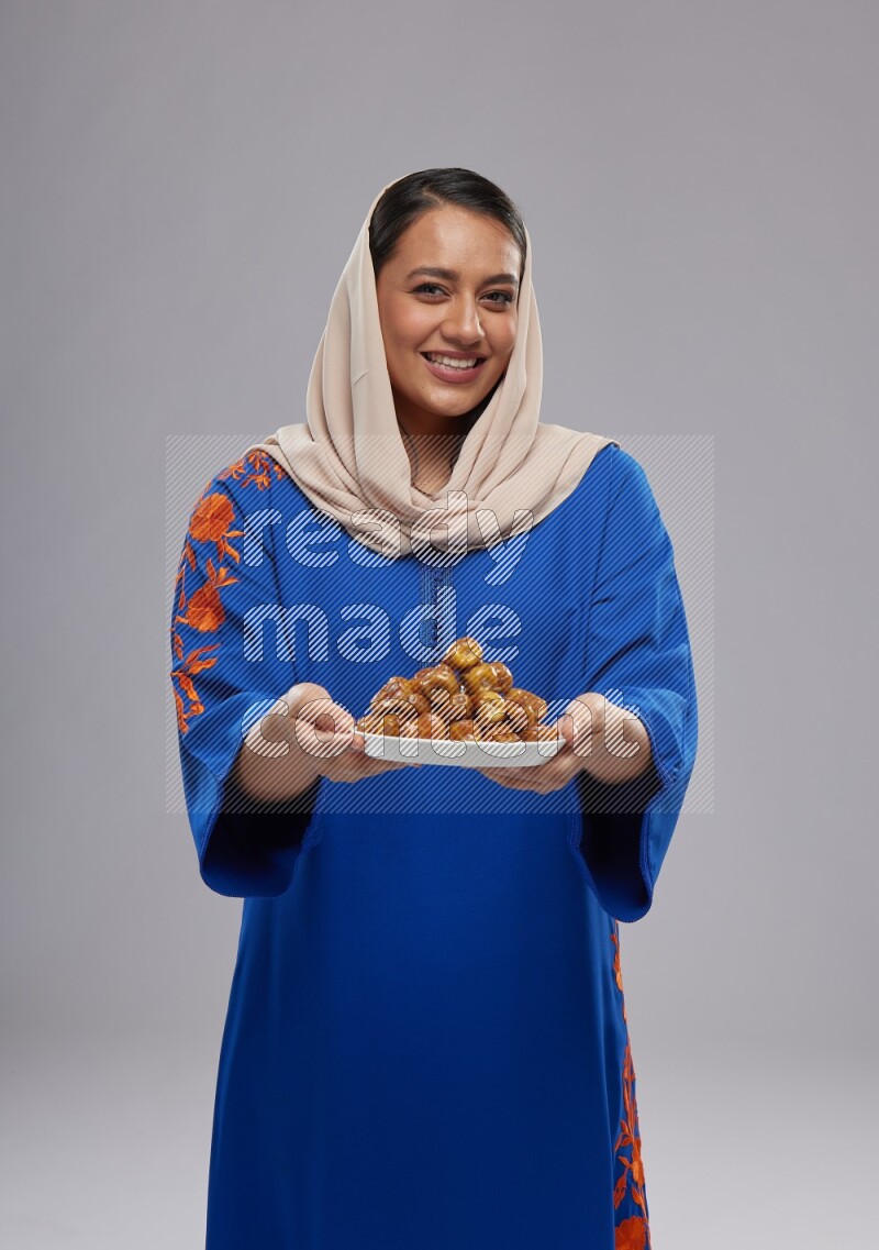 A Saudi woman standing wearing Jalabeya holding a plate of dates
