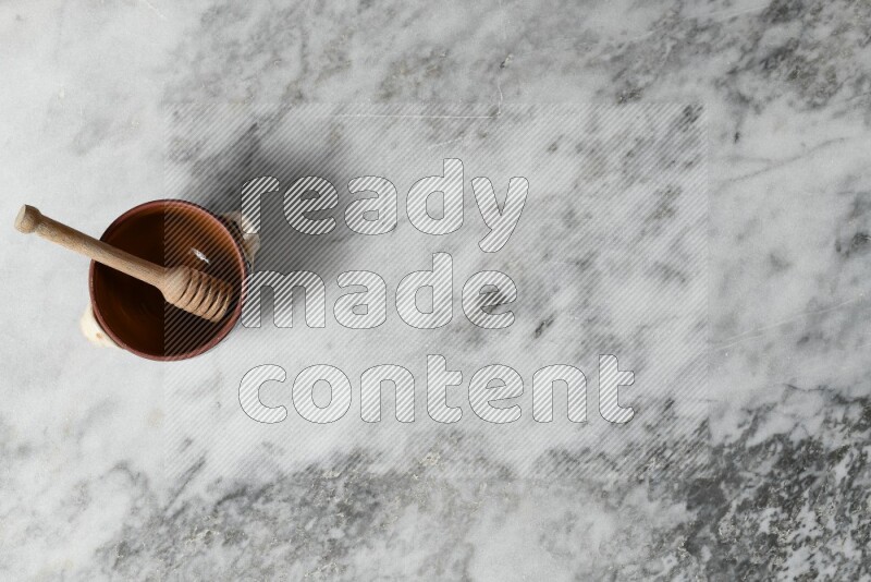 Decorative Pottery Pot with wooden honey handle in it, on grey marble flooring, Top View