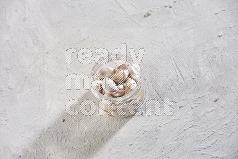 A glass jar full of garlic cloves on a textured white flooring