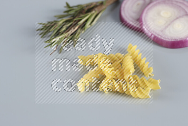 Raw pasta with different ingredients such as cherry tomatoes, garlic, onions, red chilis, black pepper, white pepper, bay laurel leaves, rosemary, cardamom and mushrooms on light blue background