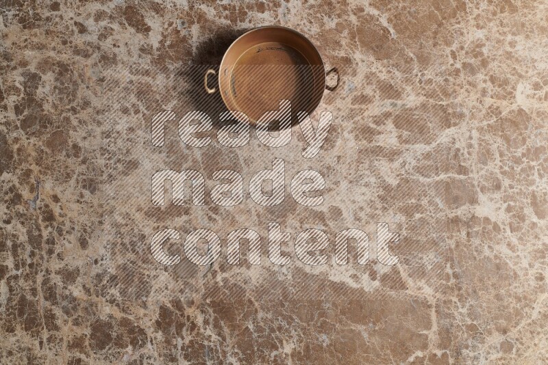 A small copper pan on beige marble background