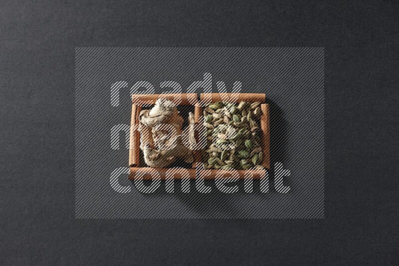 مربعان من أعواد القرفة ممتلئان بحبوب الهيل والزنجبيل المجفف علي خلفية سوداء