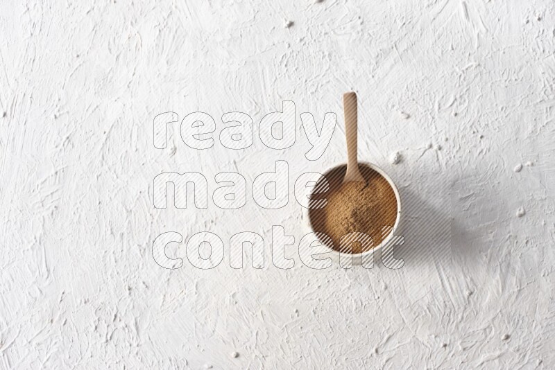 Ceramic beige bowl full of cinnamon powder with a wooden spoon on a textured white background