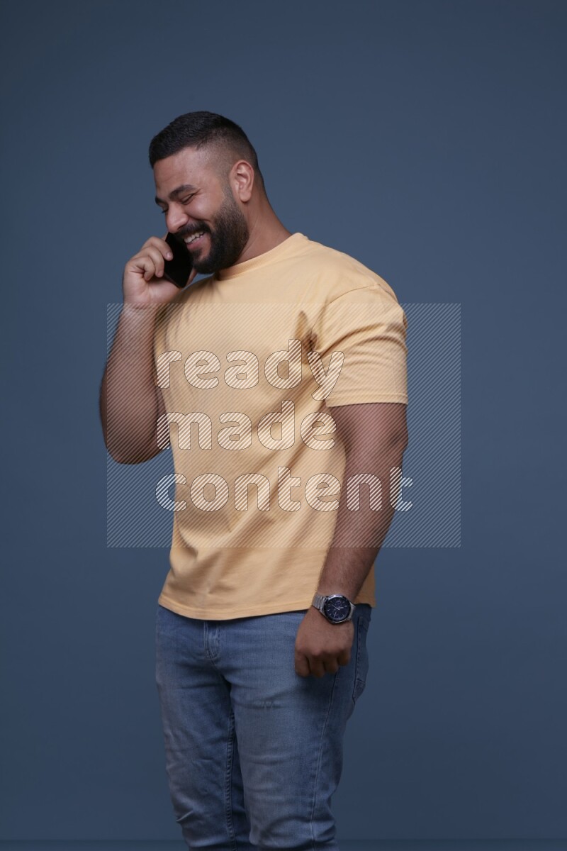 رجل يرتدي بنطال ازرق جينز وقميص اصفر بأكمام قصيره يتحدث بجواله