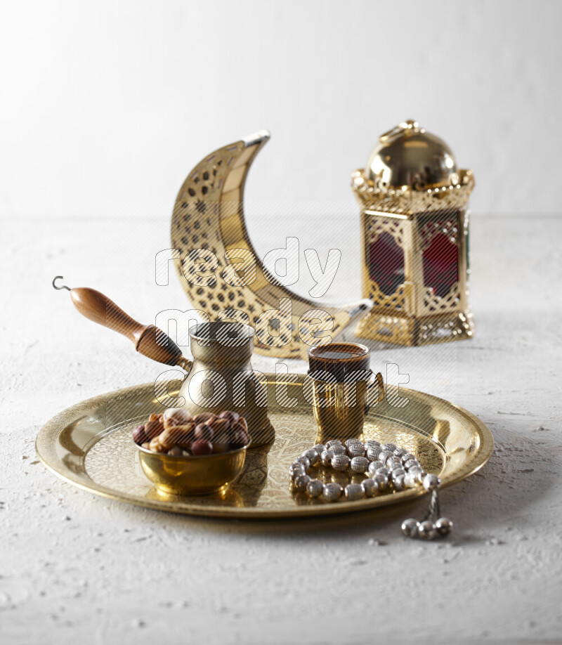 Nuts in a metal bowl with coffee and prayer beads on a tray beside lanterns in a light setup