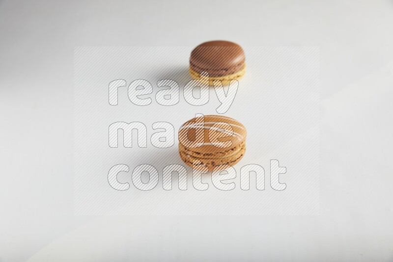 45º Shot of of two assorted Brown Irish Cream, and Yellow, and Brown Chai Latte macarons on white background