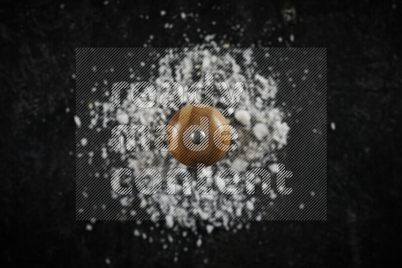 A wooden grinder standing upright and surrounded by coarse white sea salt on black background