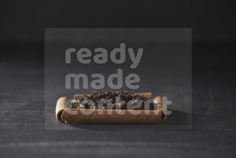 أربعة من أعواد القرفة مكونة شكل مربع بداخلها حبوب قرنفل علي خلفية سوداء