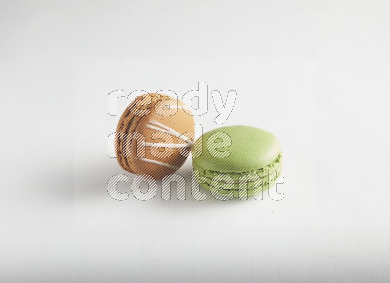 45º Shot of of two assorted Brown Irish Cream, and Green Pistachio macarons on white background