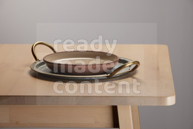 multicolored plate placed on a rounded stainless steel tray with golden handels on the edge of wooden table