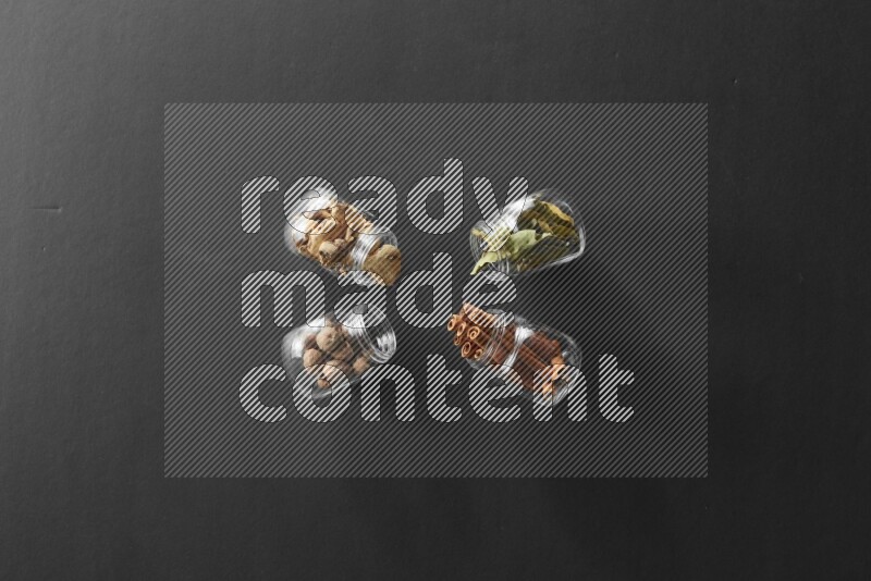 4 glass spice jars full of laurel bay leaves, ginger, cinnamon and nutmeg on black flooring