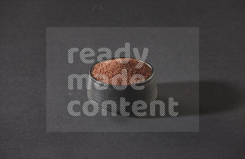 A black pottery bowl full of garden cress seeds on a black flooring