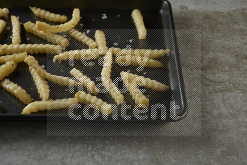 crinkle fries in a black stainless steel rectangle tray on grey textured counter top