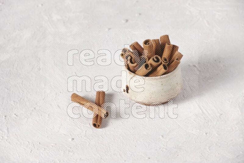 Cinnamon sticks in a beige bowl on a white background