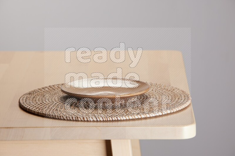 multi-colored pottery Plate placed on a big light colored straw placemat on the edge of wooden table