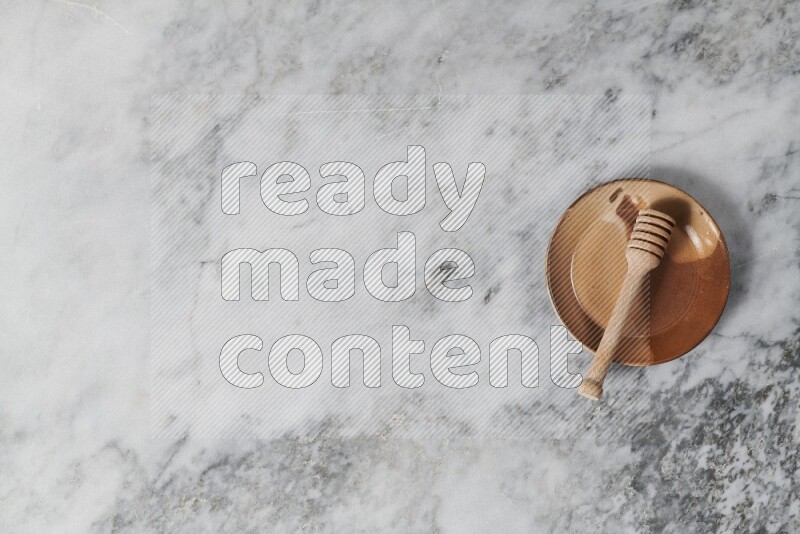 Multicolored pottery plate with wooden honey dipper in it on grey marble background