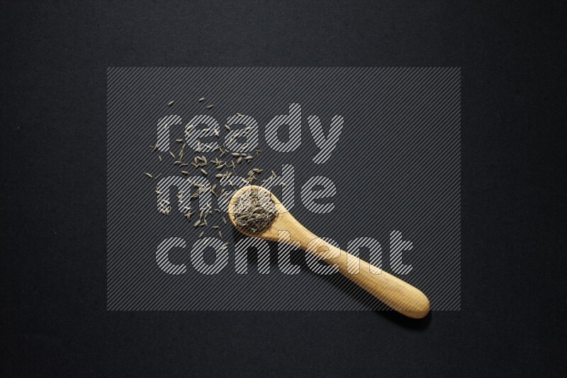 A wooden spoon full of cumin seeds on black flooring