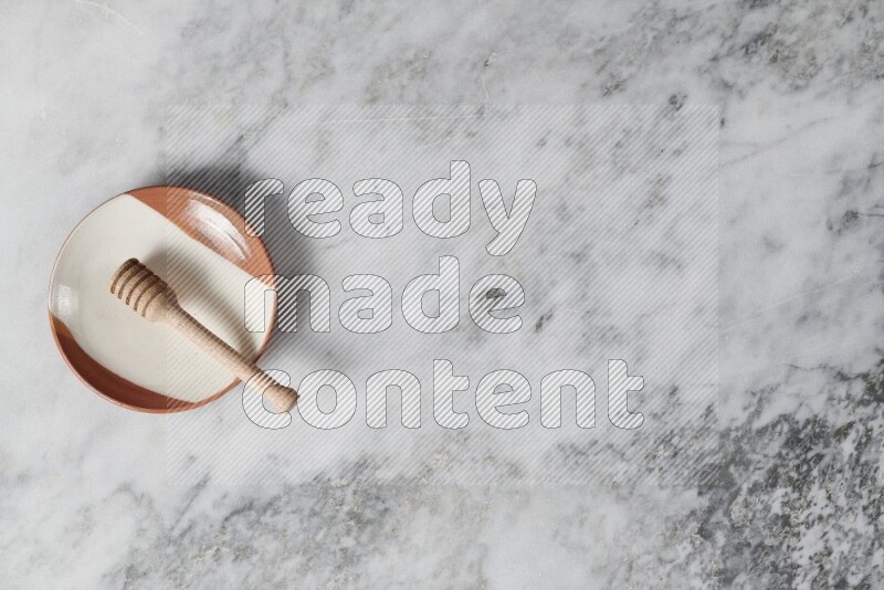 Multicolored pottery plate with wooden honey dipper in it on grey marble background