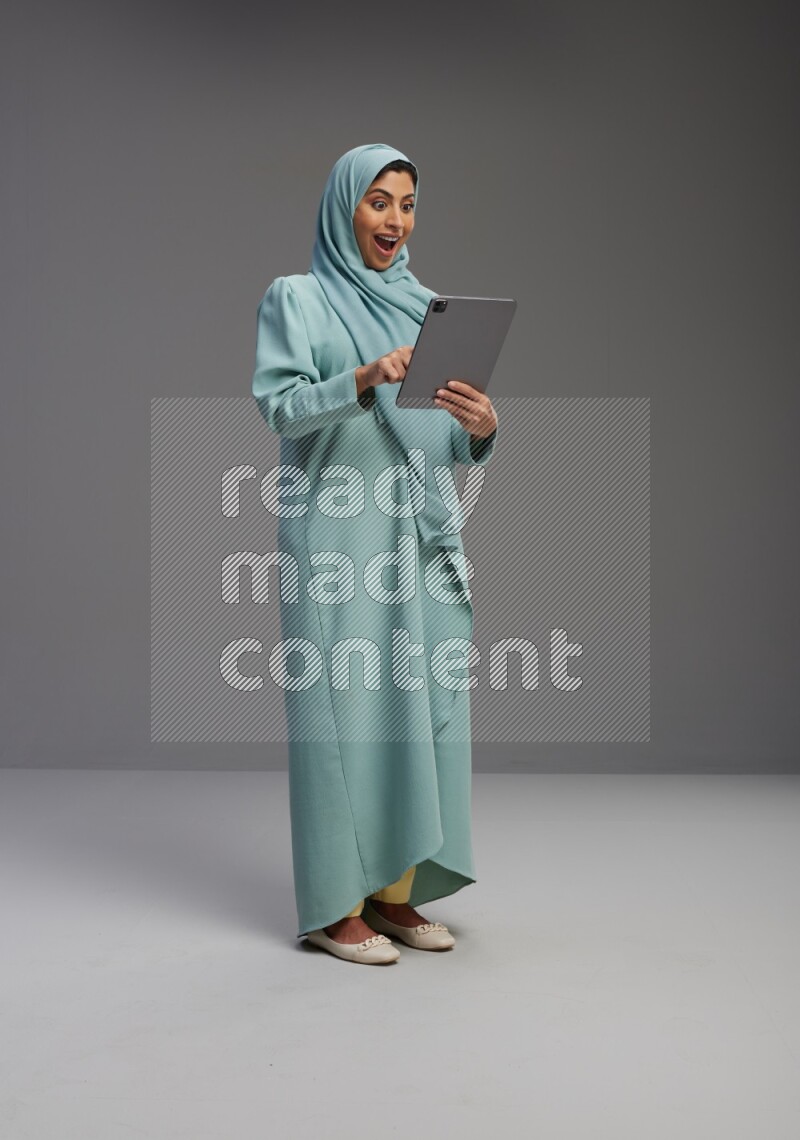 Saudi Woman wearing Abaya standing working on tablet on Gray background
