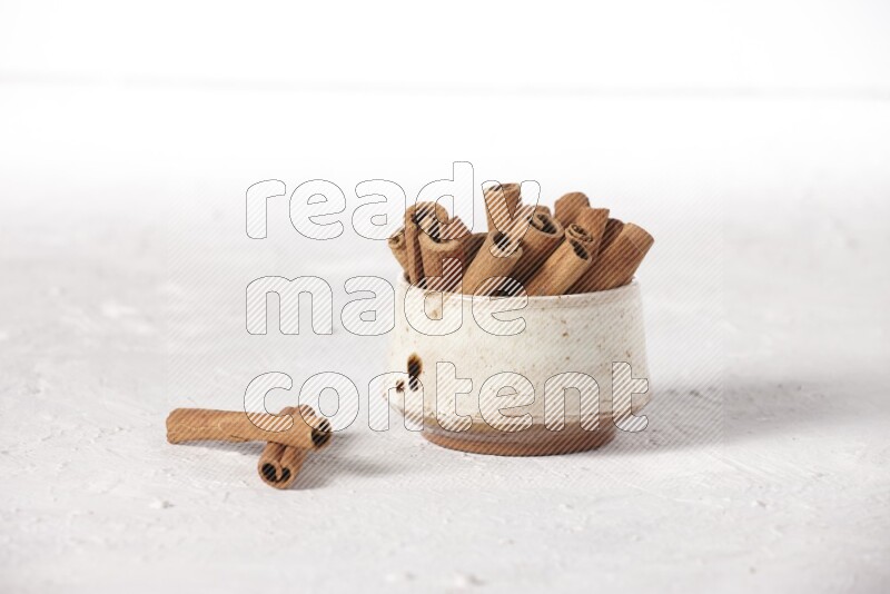 Cinnamon sticks in a beige bowl on a white background