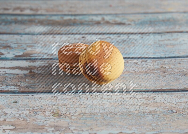 45º Shot of of two assorted Brown Irish Cream, and Yellow Crème Brulée macarons on light blue background