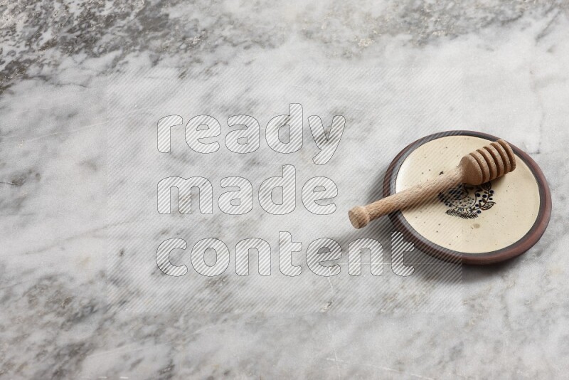 Decorative pottery plate with wooden honey dipper in it on grey marble background